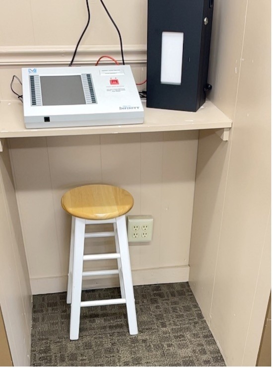 An accessible voting machine placed on a desk with a stool tucked underneath.