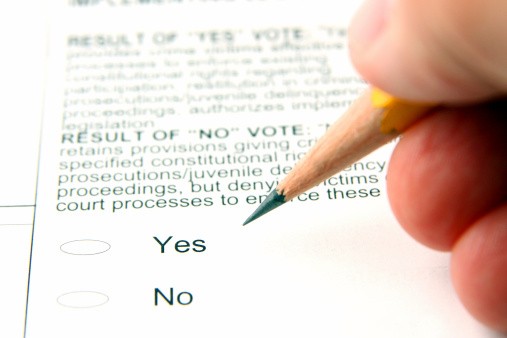 pencil held in hand above text of ballot with yes and no answers